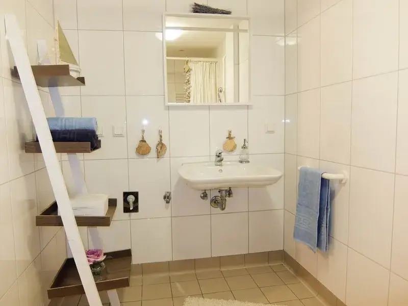 Waschecke in einem Badezimmer, links an der Wand ein offenes Regal mit Handtüchern