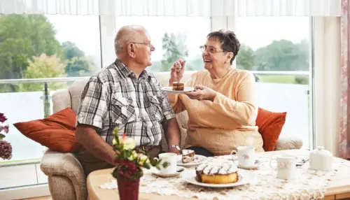 altes Paar sitzen zusammen auf einem Sofa und essen Kuchen
