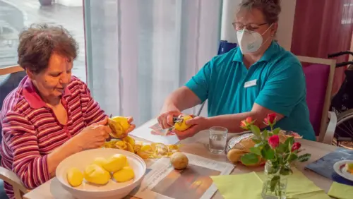 Zwei Frauen sitzen gemeinsam an einem Tisch und schälen Kartoffeln