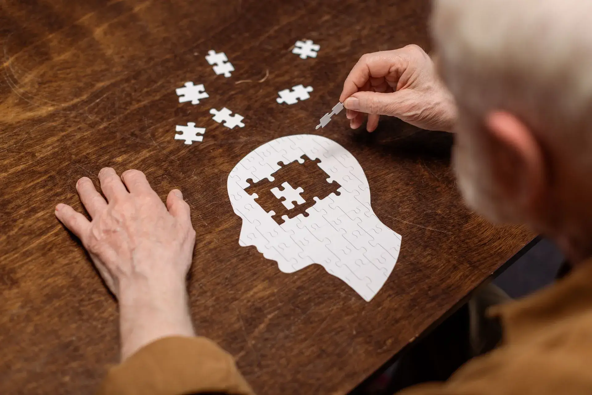 Ein Mann puzzelt ein komplett weißen Puzzle in Form eines Kopfes im seitlichen Porträt