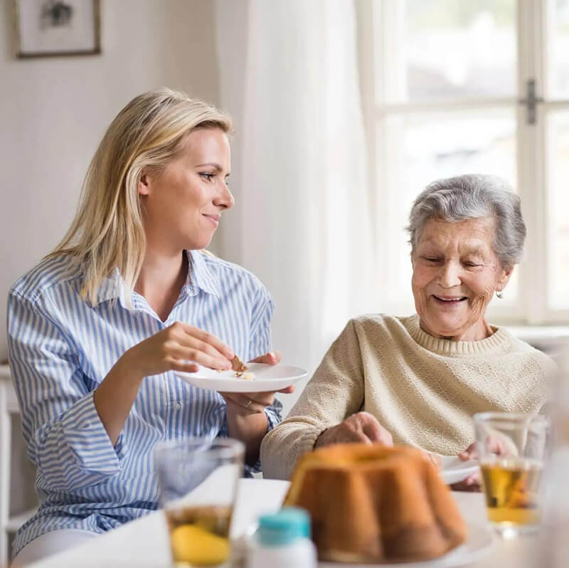 Zwei Frauen unterschiedlichen Alters sitzen zusammen am Tisch essen und lachen dabei