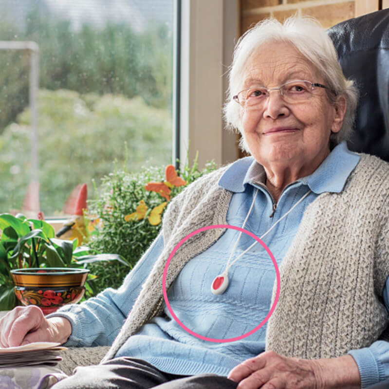 Eine alte Frau sitzt in einem Sessel. Um ihren Hals trägt sie den Hausnotruf