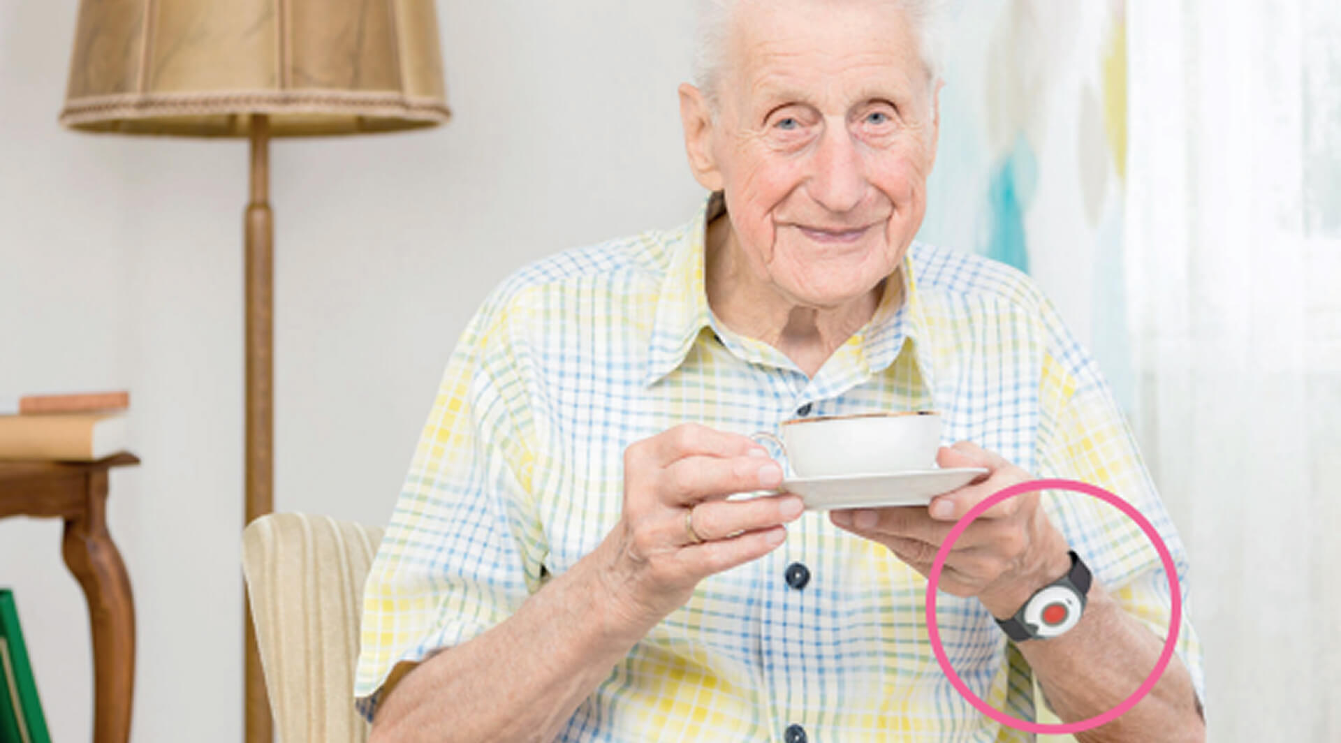 Alter Mann sitzt mit einer Tasse Kaffee in einem Sessel. Um sein Handgelenk trägt er den Hausnotruf