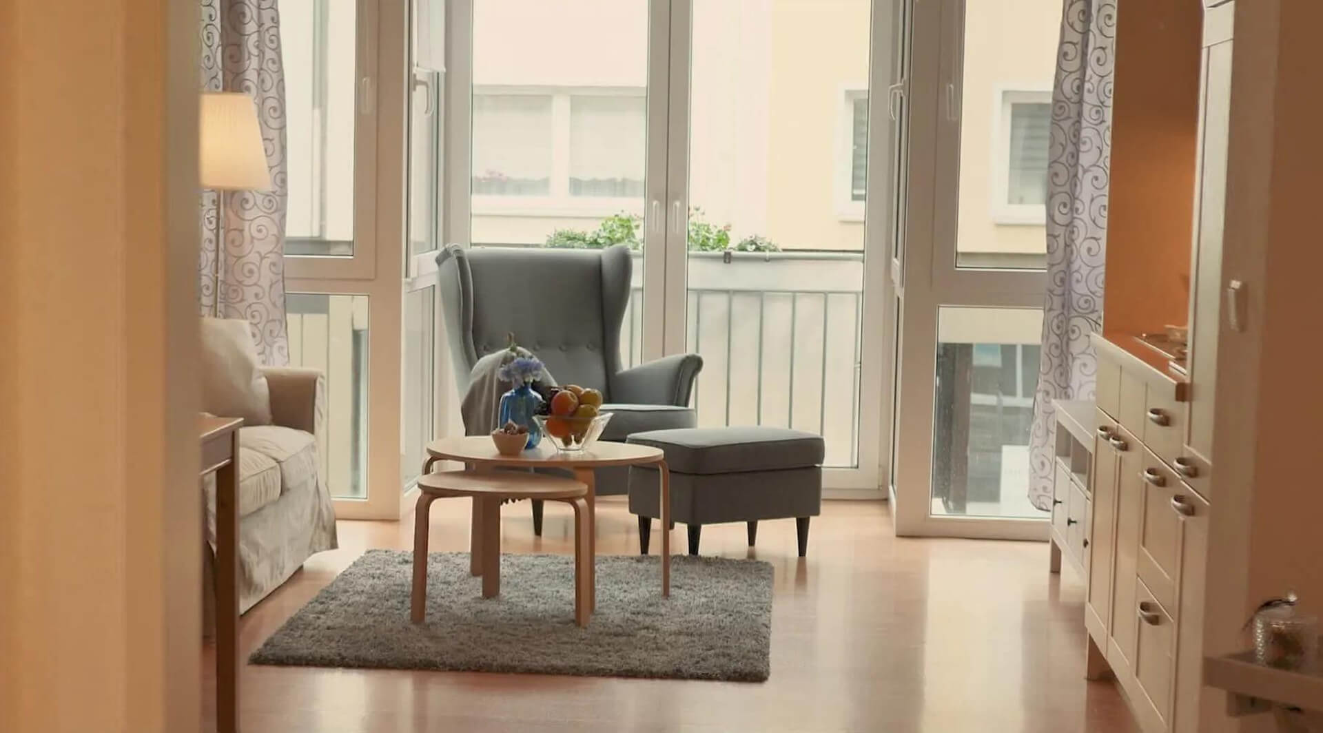 grauer Sessel mit Ottomane steht hinter einem Couchstisch vor einem Fenster mit Blick auf den Balkon