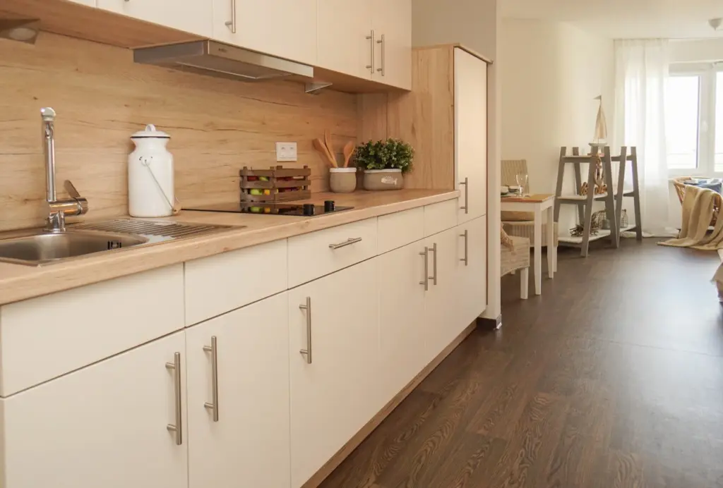 Küchenzeile in Holzoptik mit weißen Fronten, im HIntergrund Blick auf eine kleine Essecke und Bücherregal