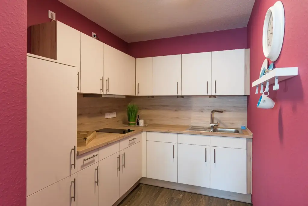 Küchenzeile in Holzoptik und weißen Fronten über Eck in einer Pink gestrichenen Küche