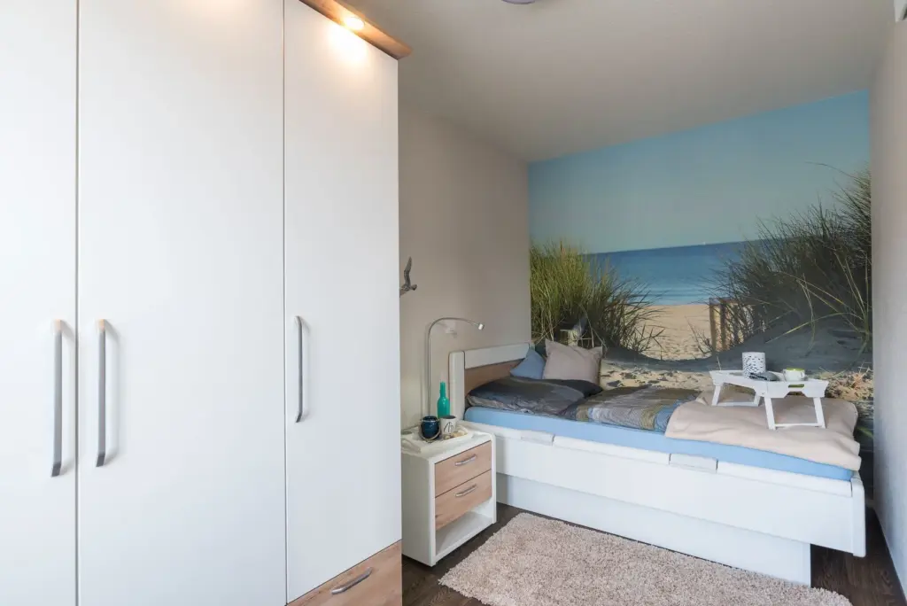 Schlafzimmer einer Wohnanlage in Bremerhaven mit Bett vor einer Wand mit Strandtapete