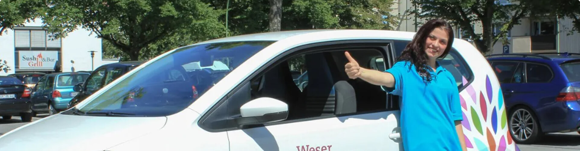 junge Frau mit ausgestrecktem Daumen nach oben steht neben einem Auto des Weser Pflegedienst