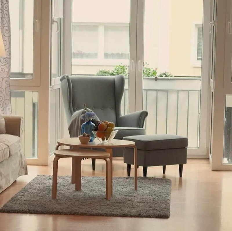 grauer Sessel mit Ottomane steht hinter einem Couchstisch vor einem Fenster mit Blick auf den Balkon